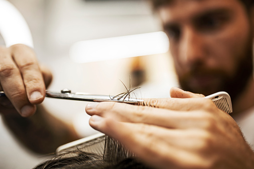 The hands of young barber making haircut to a bearded man