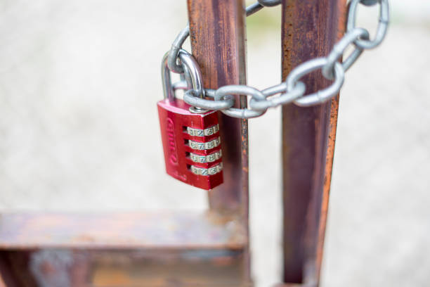 chain of metallic links around a gate locked by a red padlock with a numerical code stock photo