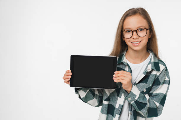 Smiling caucasian preteen teenage girl schoolgirl using digital tablet showing device screen mockup for mobile application isolated in white background stock photo