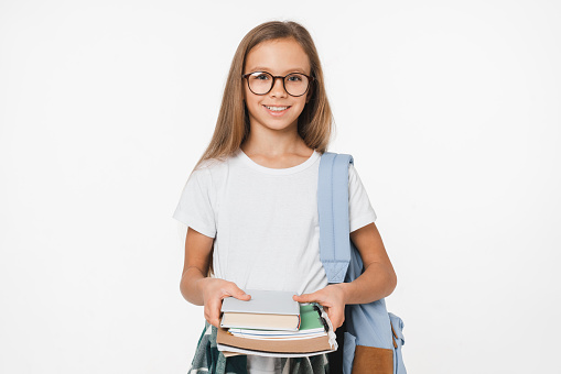 Smart young preteen schoolgirl coming back to school holding textbooks in the camera with the bag isolated in white background. Education concept