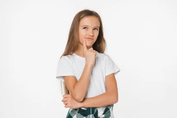 Photo of Smart small young pensive caucasian schoolgirl daughter girl in white t-shirt thinking looking dreaming looking upwards isolated in white background