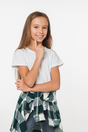 Pensive thoughtful caucasian small schoolgirl in white t-shirt and checkered looking at camera isolated in white background