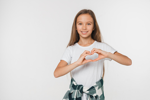 Happy caucasian young smiling teenage preteen girl showing heart shape gesture for love and care passion isolated in white background