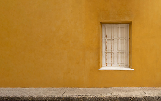 White window on panoramic yellow wall background and sidewalk. Caribbean house in cartagena.
