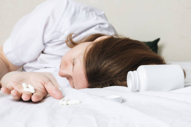 woman sleeping in bed with pills in her hands, drug overdose, drunk, fainting stock photo