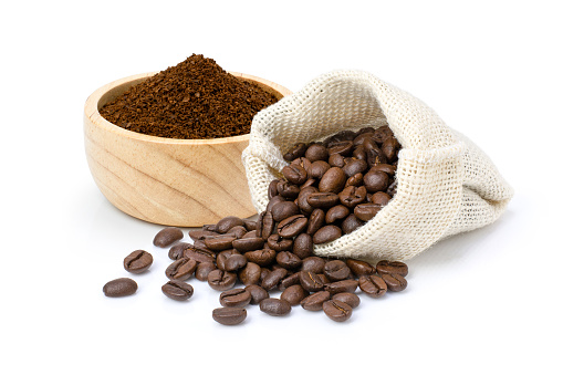 Roasted coffee beans in sack bag with coffe powder (ground coffee) in wooden bowl isolated on white background.