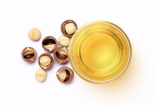 Macadamia nut and macadamia oil in glass bowl isolated on white background. Top view. Flat lay.