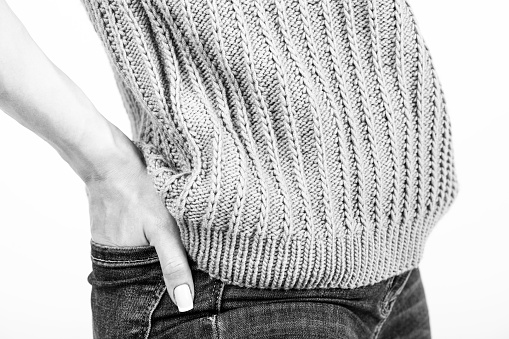 Fashion and lifestyle concept. Studio shot of beautiful and sexy woman with beautiful body shape wearing sweater and jeans. Model holding hand in back pocket of jeans. Black and white image