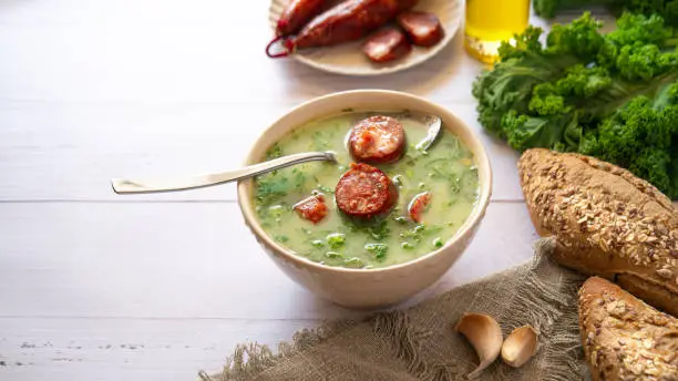 Portuguese style soup called Caldo Verde, bread, Cabbage, oil, garlic and chorizo sausage on white wooden Table. Copy space