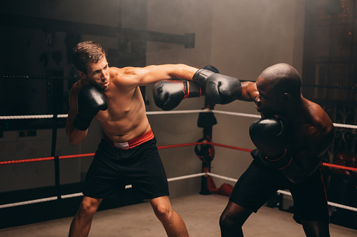 African American fighter in boxing gloves stands on ring and talks with trainer. Caucasian coach explains fighting techniques and consult boxer before competition. Physical activity and workout.