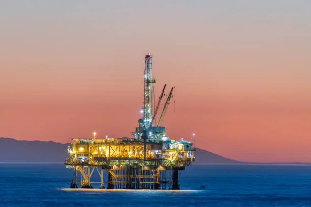 Dramatic image of an offshore oil platform off the coast of California against a pink winter sky as the sun sets and the rig's lights illuminate.