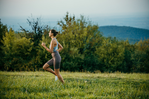 Spontaneous shot of a young woman out for a run on a mountain road, wearing a beautiful simple sportswear. Preparing for a marathon, in nature