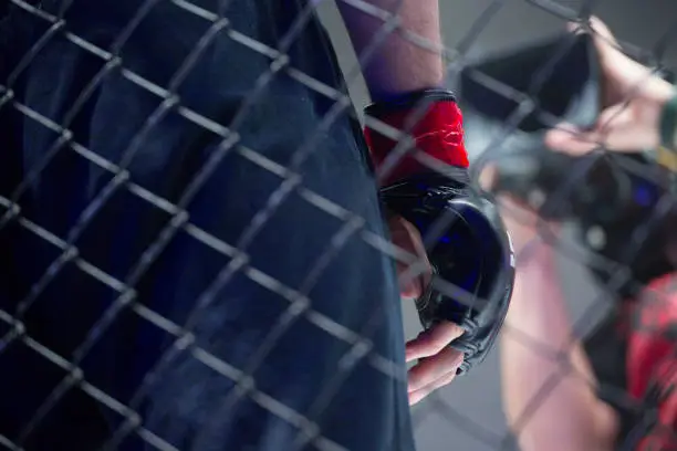 The concept of mixed martial arts. MMA.  close up hand and cage is a metal wire, in the background the arena is an octagonal stage of fights