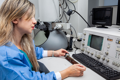 Young female scientist loading a grid with an specimen on the sample holder of a transmission electron microscope