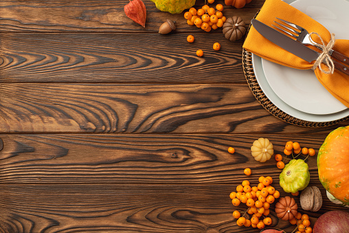 Thanksgiving day concept. Top view photo of table setting plate knife fork napkin vegetables pumpkins pattypan squash walnut acorn physalis rowan isolated dark wooden table background with copyspace