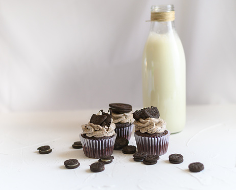 Three homemade chocolate and cookie cupcakes next to a bottle of milk on white background. Homemade chocolate biscuit muffins next to bottle of milk on isolated background
