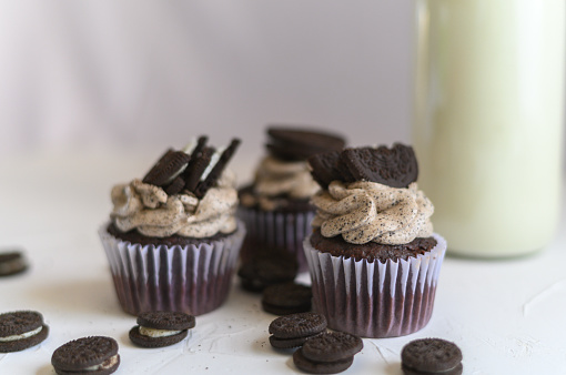 Chocolate muffins with cookie pieces on top. Close up of three chocolate cupcakes with cookie on top on white background. chocolate cupcakes with cookies and a bottle of milk