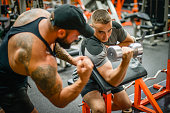 Man doing exercises in the gym with a man trainer athletic physique