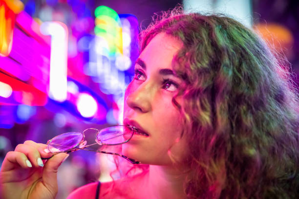 tourist amazed by the neon lights at Soi Cowboy - red light district in Bangkok Young tourist woman amazed by the neon lights at Soi Cowboy - red light district in Bangkok. distracted biting her glasses. Thailand strip club stock pictures, royalty-free photos & images