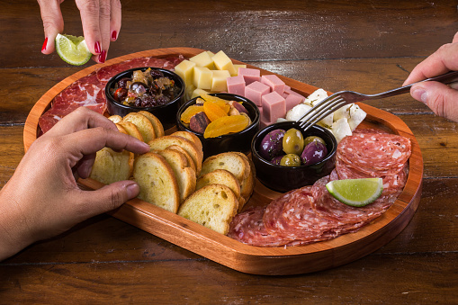 People eating wooden cutting board with cheese, cold cuts and jams.