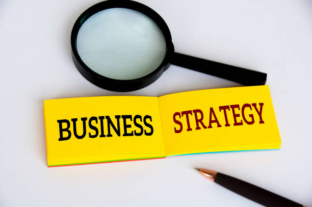 istock Business strategy text on yellow notepad with magnifying glass and pen on white background. Business strategy concept 1422816522
