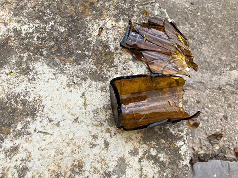 Shattered brown beer bottle resting on the ground: alcoholism concept - toned image