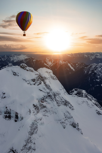Dramatic Mountain Landscape covered in clouds and Hot Air Balloon Flying. Adventure Composite Dream Concept Artwork. Aerial Image from British Columbia, Canada. Colorful Sunset Sky