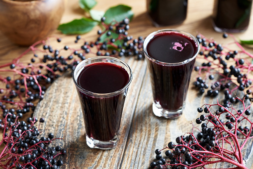 Two shot glasses of homemade black elder syrup with fresh elderberries on a table