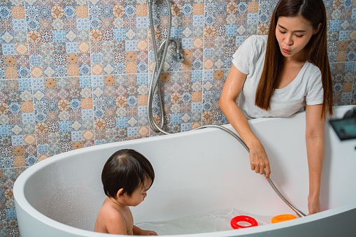 Asian young mother bathing the cute little son with toys for her son to play in the tub.