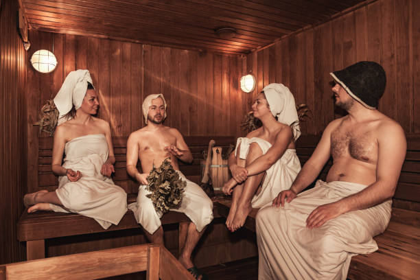 bains publics russes. deux couples se détendent et transpirent dans un sauna en bois avec de la vapeur chaude. quatre personnes avec besoms de bain reposant sur un banc dans le complexe spa. bien-être, soins personnels, concept sain. copier l’espace de - health spa couple spa treatment towel photos et images de collection