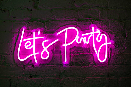 Lets party pink glowing neon sign banner on brick wall