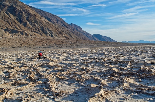 A couple work over a camera to photograph the vast wasteland of the bad water section of Death Valley national park. Image from the fall of 2009. The salt and mineral deposits challenge any hiker but provides a beautiful stark landscape.