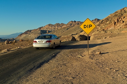 Road sign warning of a dip in the road with car on the desert road in the southern portion of Death Valley national park California. Image from the fall of 2009.