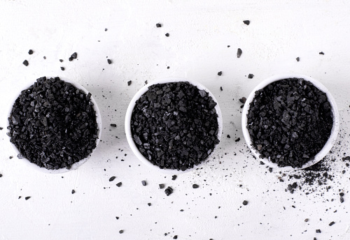 Black lava salt in small bowls on white table. Top view
