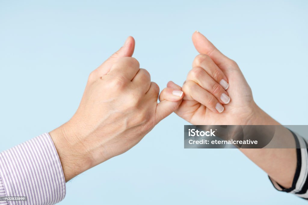Two people making a bet in front of a blue background Making a bet. Two people making a bet in front of a blue background. close-up of hand gestures Pinky Promise Stock Photo