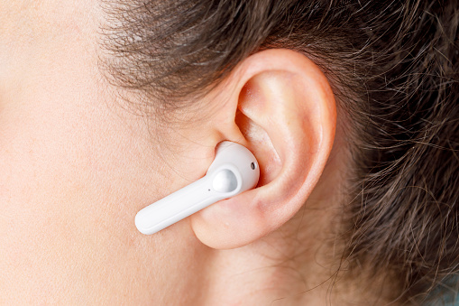 Close-up of a white white wireless earphone in a girl's ear