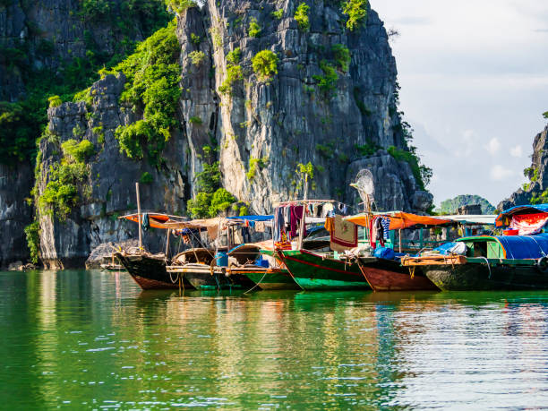 Multicolored fishing boats reflected in the emerald waters of Ha Long bay, Vietnam stock photo