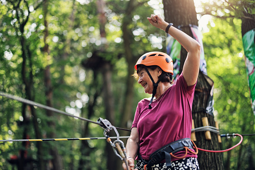 Senior woman is enjoying high ropes course in adventure park. \nSunny summer day.\nCanon R5