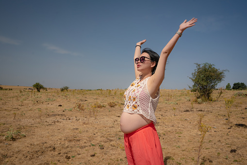 outdoors lifestyle portrait of young happy and beautiful Korean woman enjoying summer holiday while pregnant proud of her belly as mother expecting baby concept