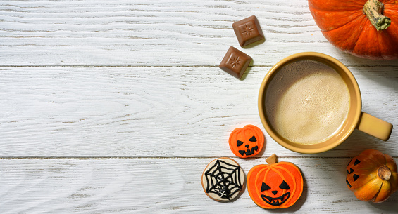 Halloween and coffee theme, orange pumpkin, sweets and cup on white table, top view. Holiday food on wood planks background with space, flat lay. Party, season, October, tasty and breakfast concept.