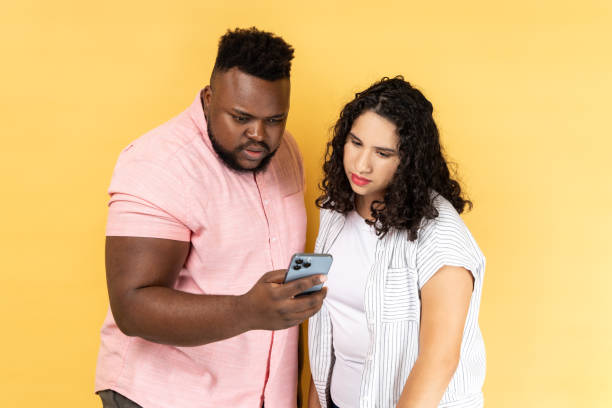 istock Concentrated young couple using mobile phone, looking at display, checking social networks. 1422843596