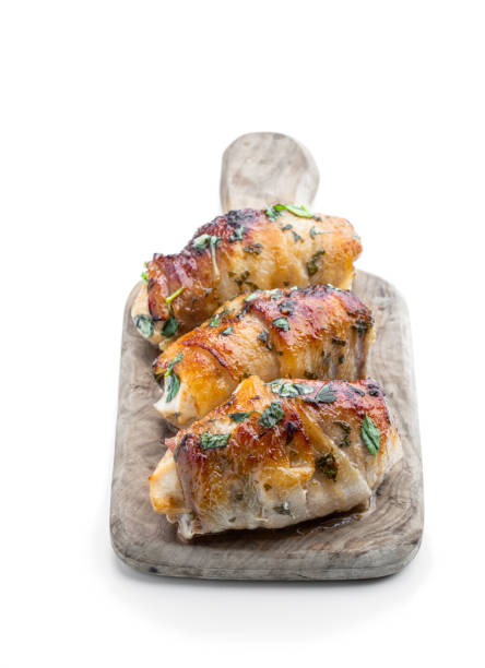 istock Chicken breasts wrapped in bacon on wooden board isolated on white 1422843879