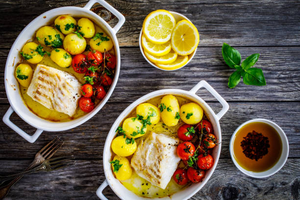 istock Cooked cod steak, potatoes and cherry tomatoes served in ceramic pan on wooden table 1422847218