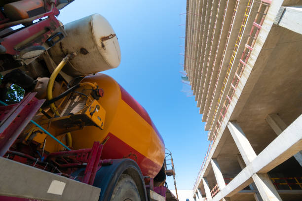primo piano di un camion betoniera si trova accanto a un grande edificio in costruzione in una giornata di sole. vista dal basso verso l'alto - mescolatore di cemento foto e immagini stock