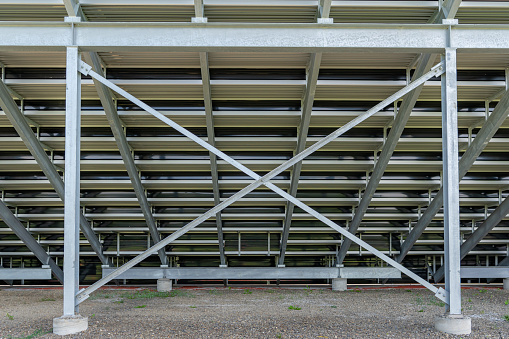 Straight on view of under stadium bleachers, steal I-Beam bleachers with X cross brace, with stone surface.\tNondescript location with no people in image.  Not a ticketed event.