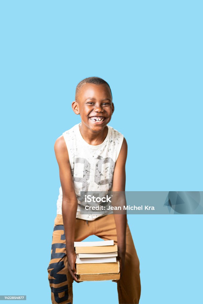portrait with blue background of a young student boy holds all books with happiness Child who used books with great enthusiasm African Ethnicity Stock Photo