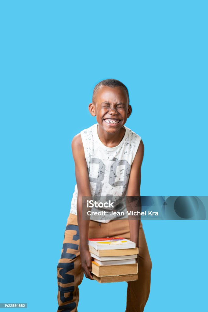 portrait of a young black boy isolated with blue background raising books with faticca Child who used books with great difficulty African Ethnicity Stock Photo