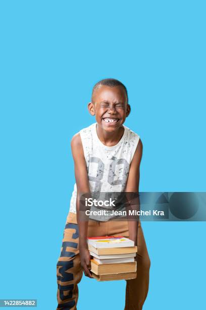 Portrait Of A Young Black Boy Isolated With Blue Background Raising Books With Faticca Stock Photo - Download Image Now
