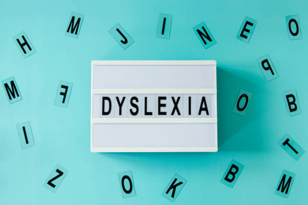 White lightbox with DYSLEXIA word and different letters haphazardly scattered on light blue background. Top view