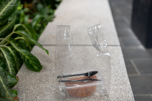 Image of a plastic bag with plastic box with bun and croissant with plastic fork and spoon outdoor